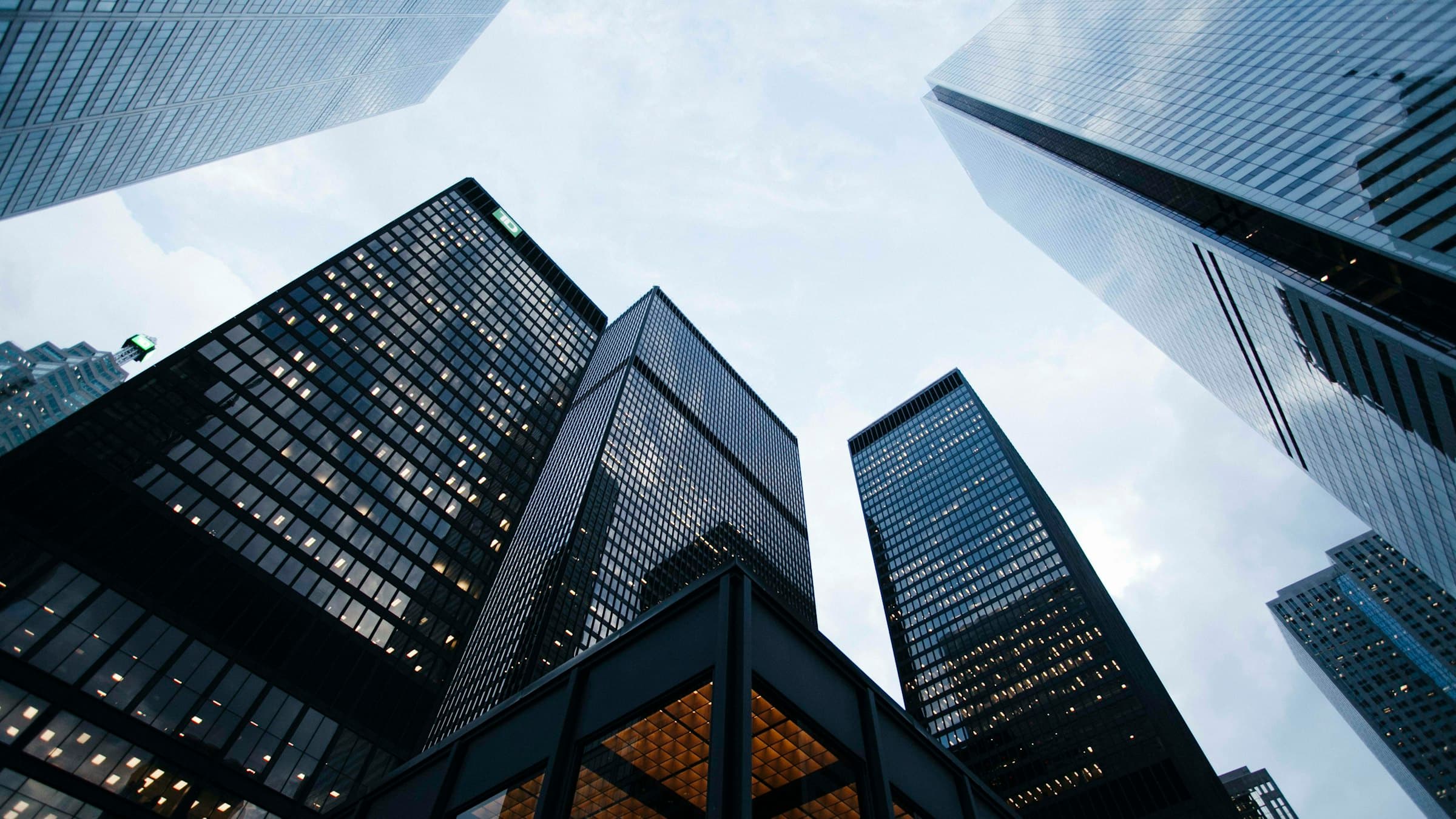 The towers of a financial district seen from below, glass facades lit at dusk.